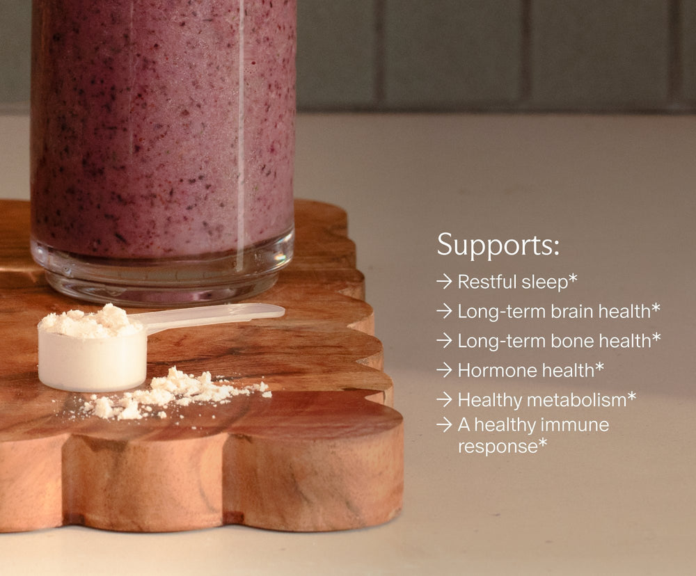 Perimenopause Multivitamin vanilla powder scoop beside a berry smoothie. Supports: restful sleep, long-term brain health, long-term bone health, hormone health, healthy metabolism and a healthy immune response.