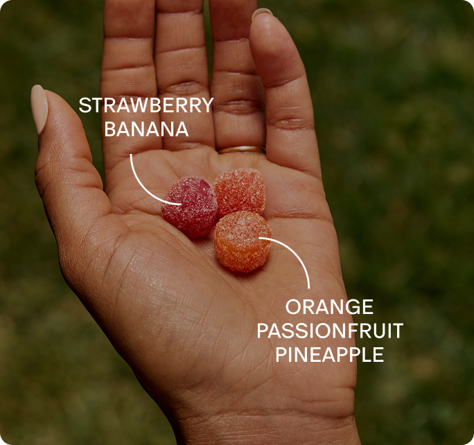 An open hand holding two Needed gummies, labelled strawberry banana and orange passionfruit pineapple