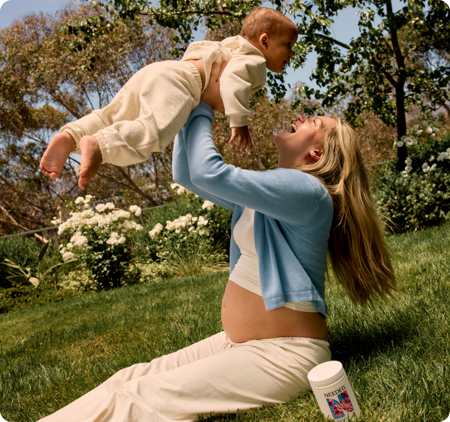 A mother lifting her baby overhead in a sunlit garden