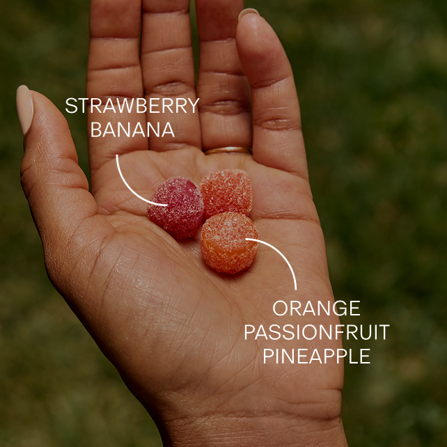 Gummies in an open palm, labelled strawberry banana and orange passionfruit pineapple