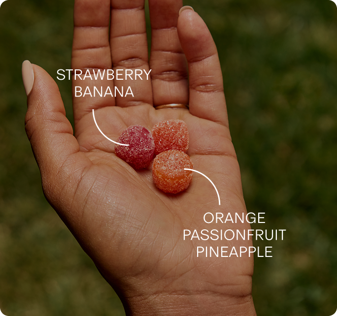 Three gummies in an open palm, labelled Strawberry Banana and Orange Passionfruit Pineapple