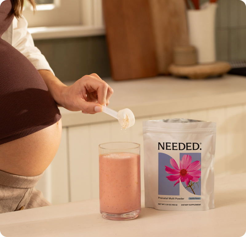 Person scooping Needed Prenatal Multi Powder into a glass beside the pouch