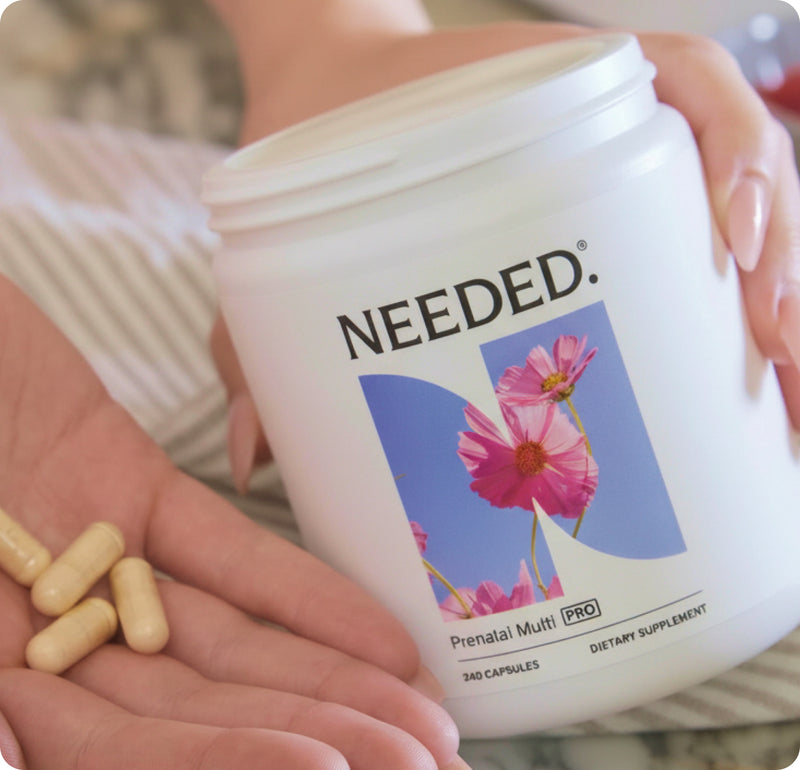 Hands holding a jar of Needed Prenatal Multivitamin Pro with capsules